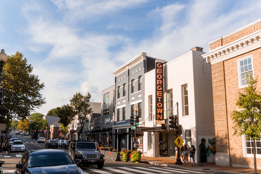 Pedestrians and cars pass by storefronts under a bright Georgetown sign on a bustling street in the historic Georgetown neighborhood of 라이브카지노, DC.